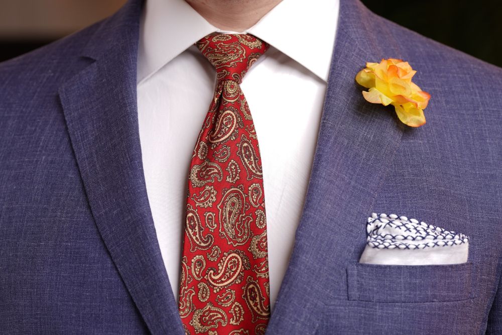 Peach Spray Rose Boutonniere combined with white pocket square and red paisley tie in blue suit