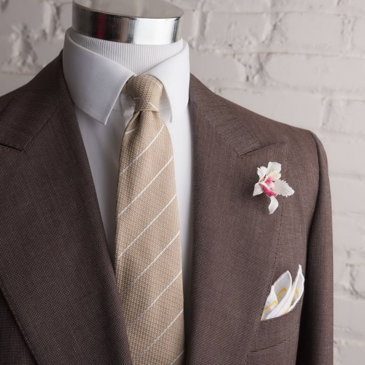 Beige jacquard silk tie with orchid boutonniere and white linen pocket square by Fort Belvedere