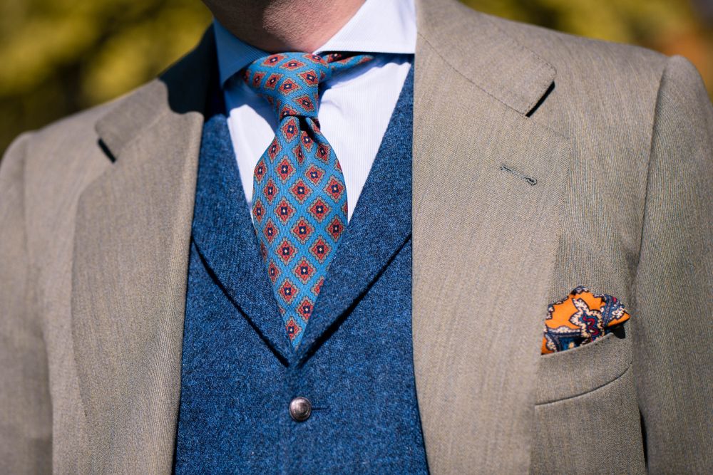 Wool Challis Tie in Turquoise with Gray, Orange, Navy and Yellow Pattern in white long sleeve, blue vest and light gray suit with Antique Gold Ochre Silk Wool Pocket Square with Printed geometric medallions in beige, red and blue with cream contrast edge 