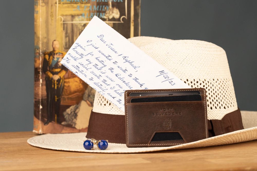 Lifestyle shot with book, slim wallet in Montecisto leather by Fort Belvedere and Panama hat, letter and cufflinks.