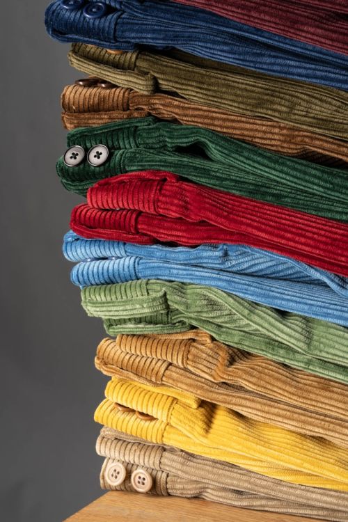 Stack of 11colors of Corduroy Trousers, Model Stancliffe by Fort Belvedere casually stacked on top of each other with visible belt loops and buttons